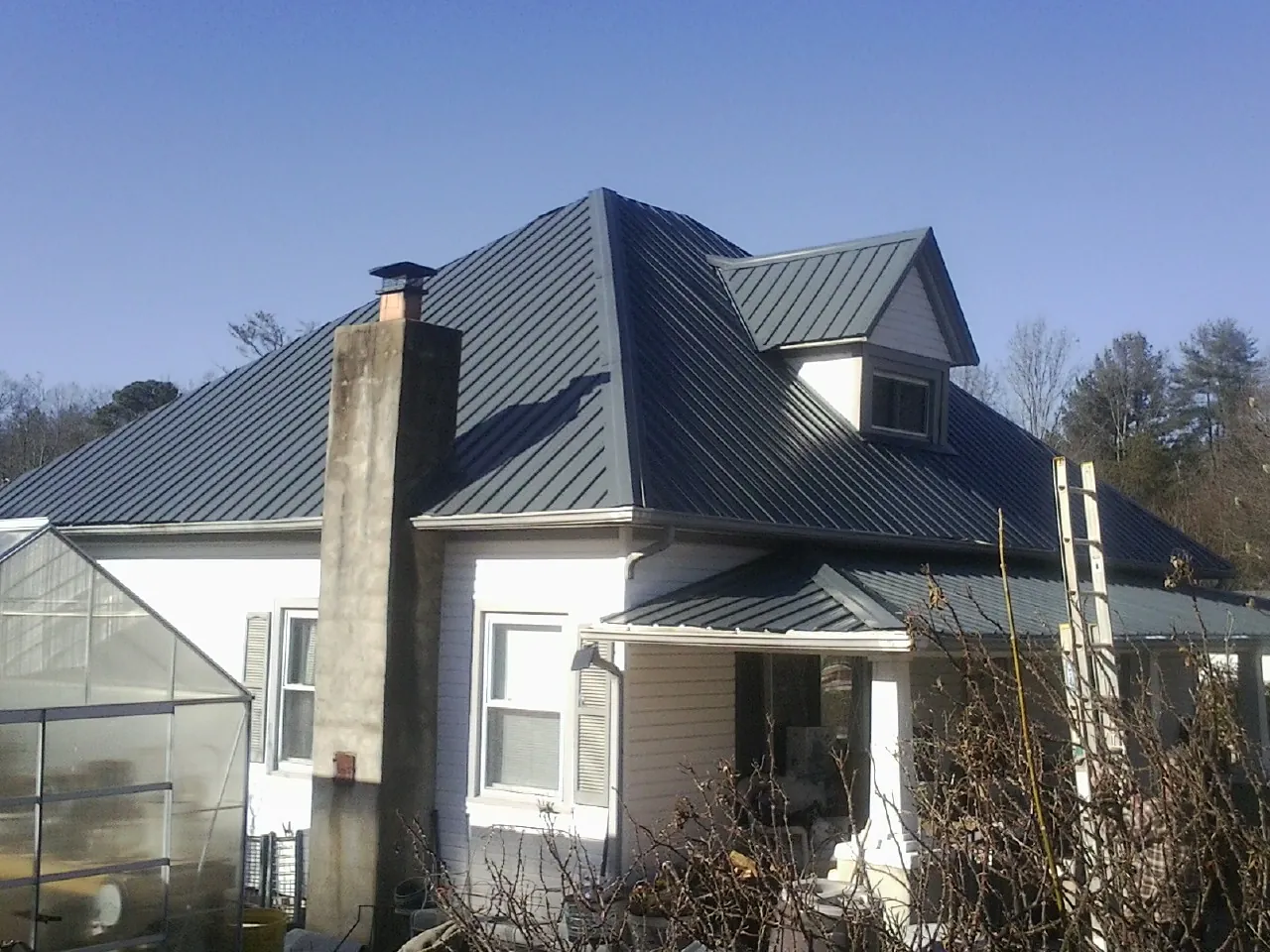 Dark blue standing seam metal roof on a white farmhouse with dormer — Slate & Tile Roof Repair by Roofing Brothers in Fayville