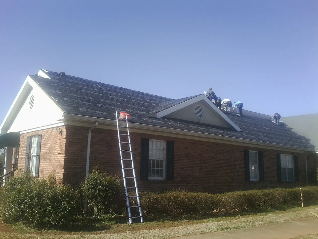 Crew tearing shingles off a brick ranch roof with a ladder set — Emergency Roof Repair work by our crew in Fayville
