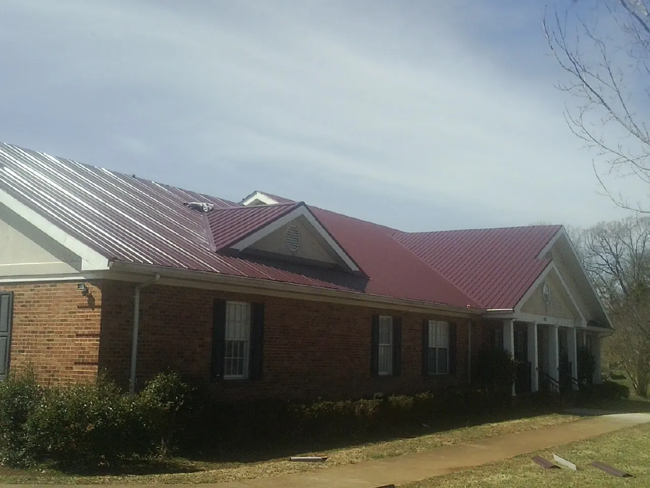 Red metal roof with gabled entries on a long brick building, from a Hail Damage Roof Repair job in Fayville
