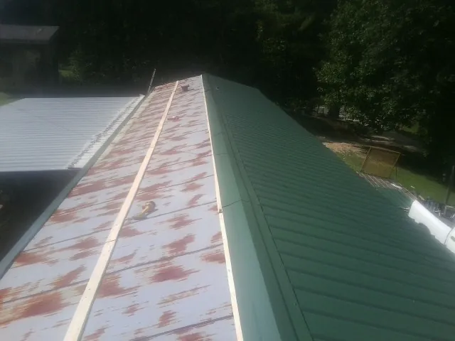 Old rusted panels beside newly installed green metal roofing — Wind Damage Roof Repair by Roofing Brothers in Fayville