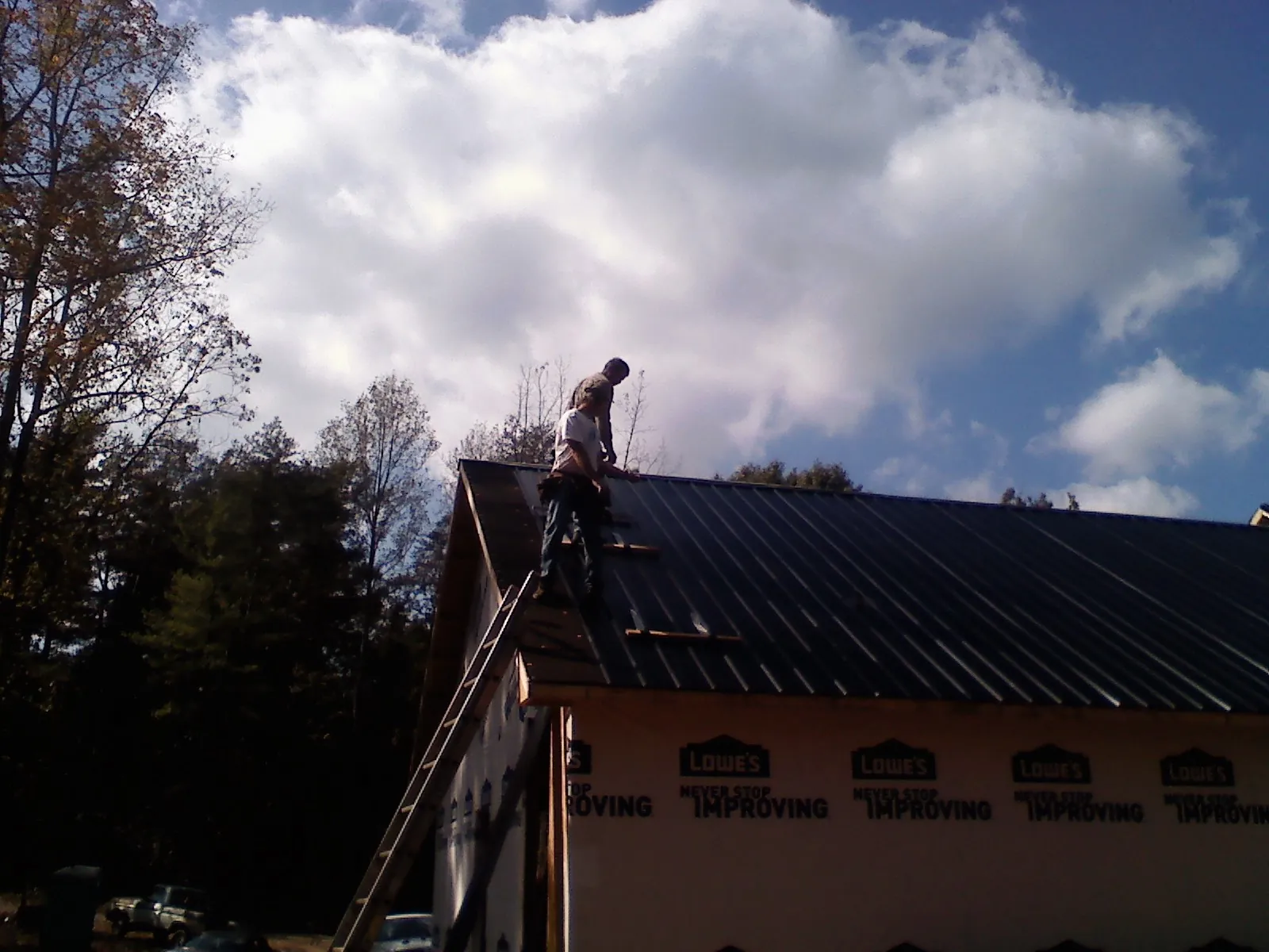 Roofer fastening dark metal panels high against a cloudy sky, from a Roof Inspection job in Fayville