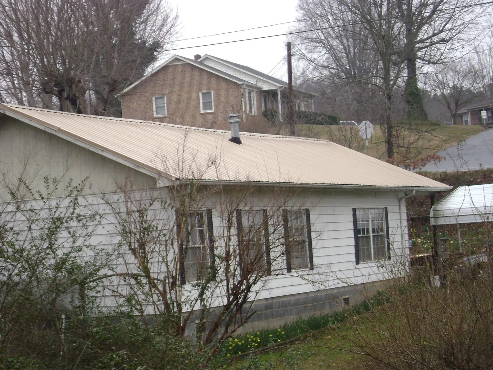 Tan metal roof on a white sided house set into a hillside — Commercial Roofing by Roofing Brothers in Fayville
