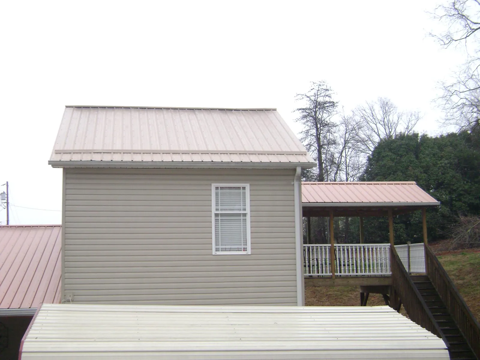 Tan metal roofs on a two story addition and attached porch, from a Roof Replacement job in Fayville